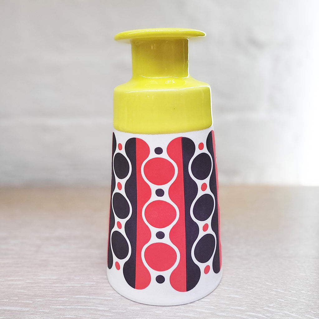 Slab-built porcelain ceramic bottle by Contemporary Ceramicists MapMap. Has a distinctively mid-centurary modern feel - this piece is predominently white background with navy and red pattern and a yellow top section.
