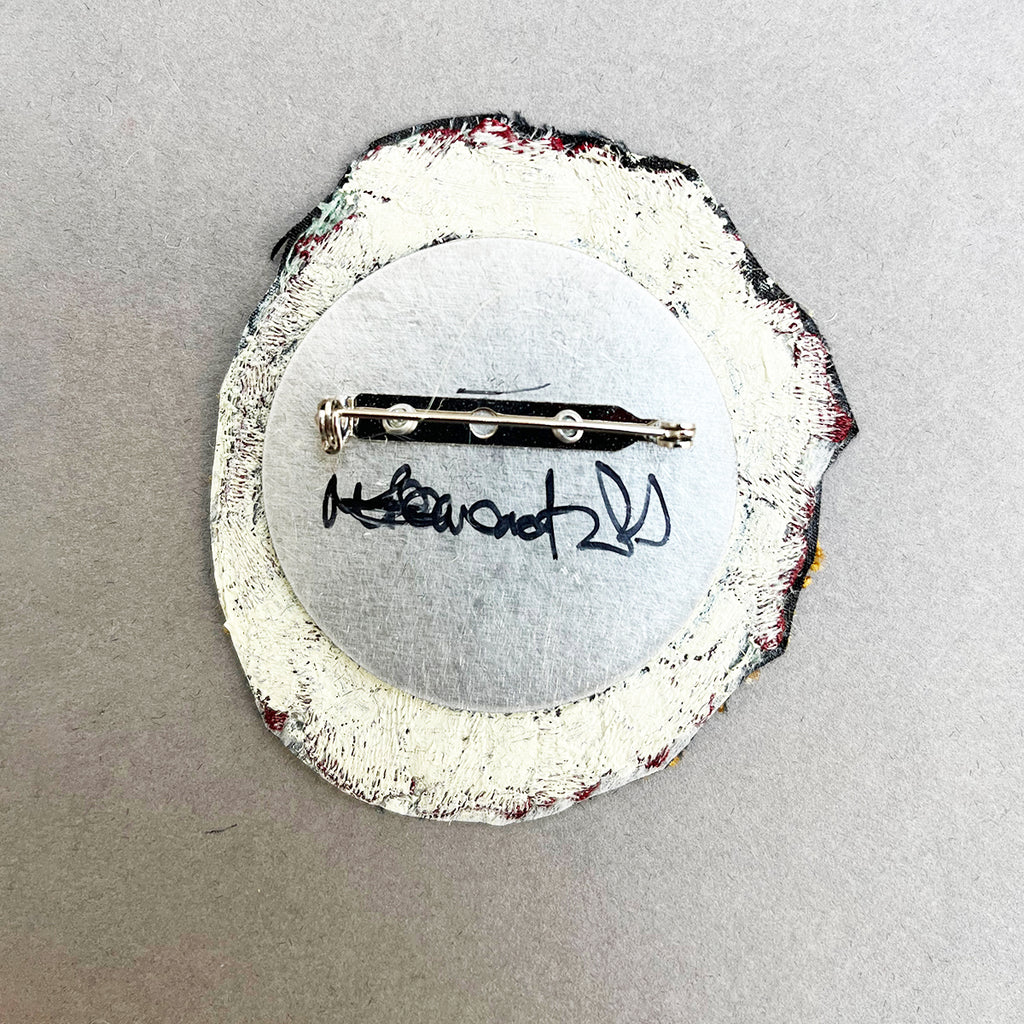 rear view of machine embroidered brooch depicting a blue and burgundy skull by Michael Brennand -Wood, showing the artist's signature