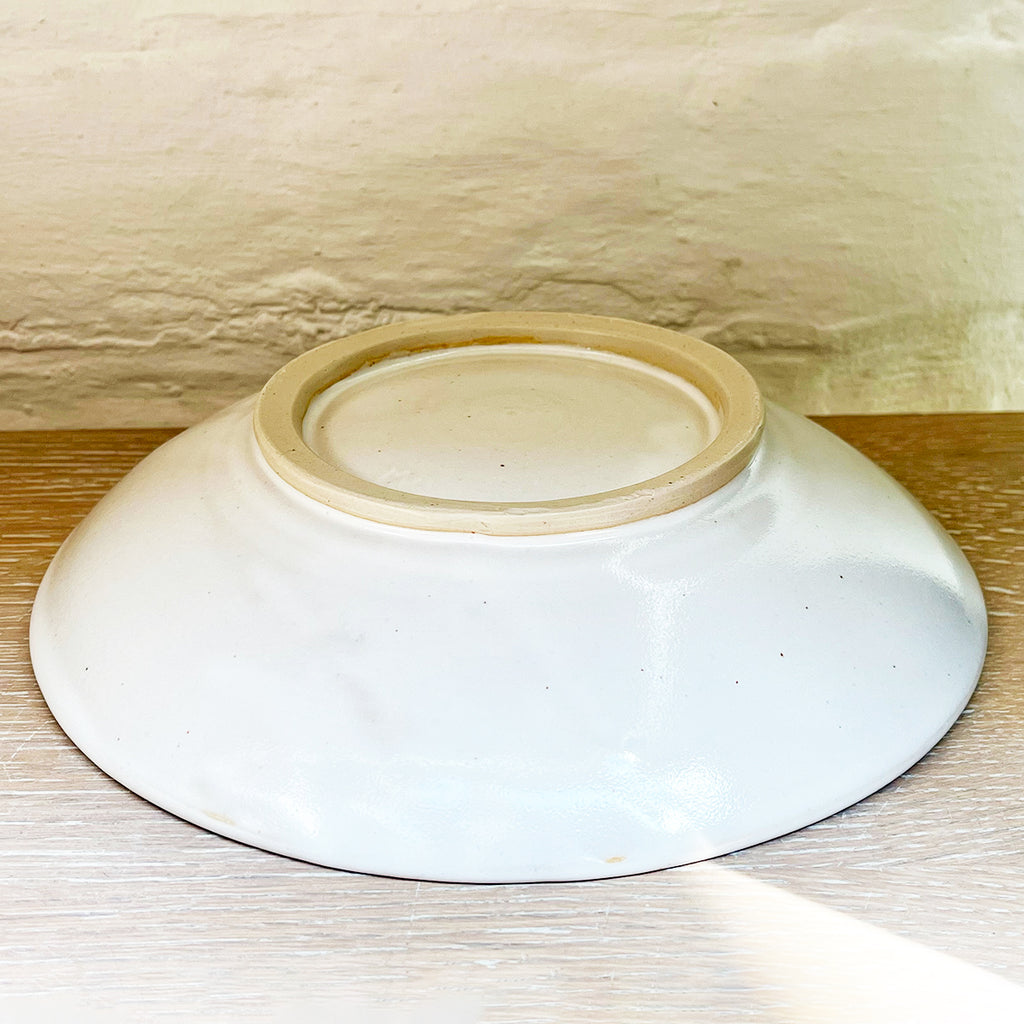 the base of A beautiful round serving dish made from white-glazed stoneware and hand decorated with two cobalt blue fish.