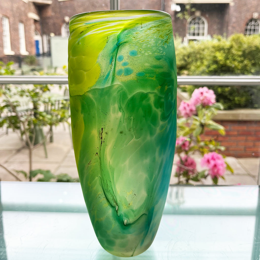 Green glass vase from Will Shakspeare's 'Random Trails' range, inspired by walking in the Elan Valley in Wales.  This vase is predominently green with varying shades, plus blue and yellow highlights shown insitu in the Bluecoat  Display Centre