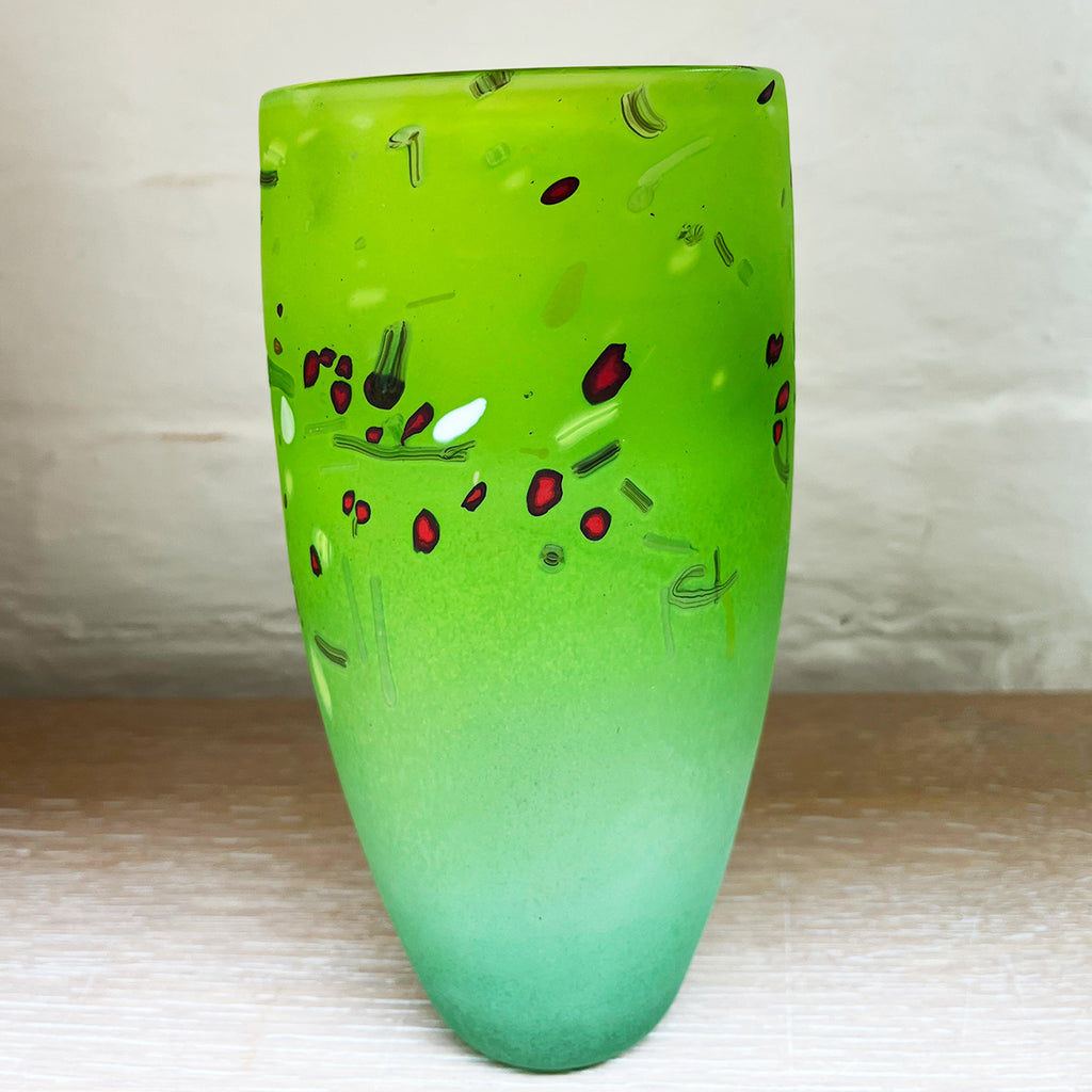 a view of medium cone vase by contemporary glass artist Will Shakspeare. The piece is inspired by the landscape of the Somerset Levels and is predominantly green in colour with accents in red, black and white