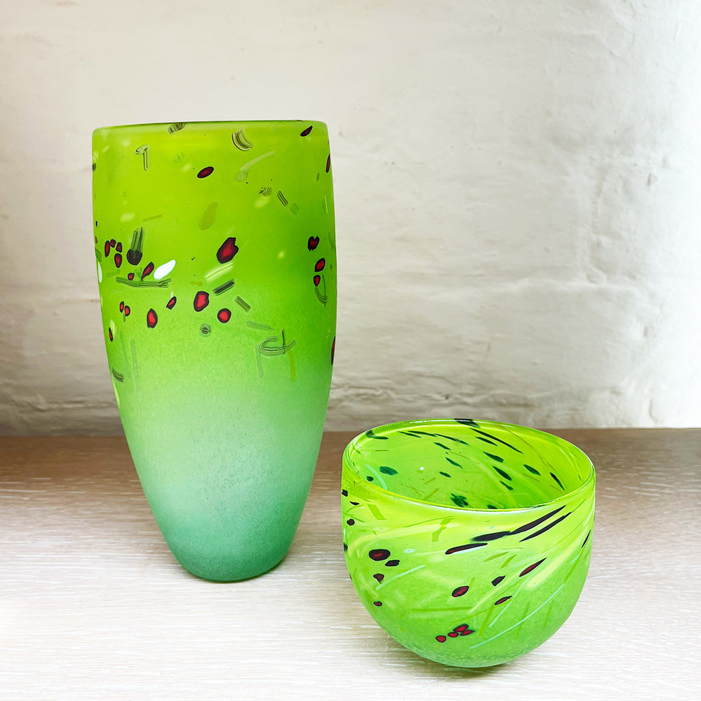 A medium cone vase next to a small bowl by contemporary glass artist Will Shakspeare. Pieces inspired by the landscape of the Somerset Levels and  predominantly green in colour with accents in red, black and white