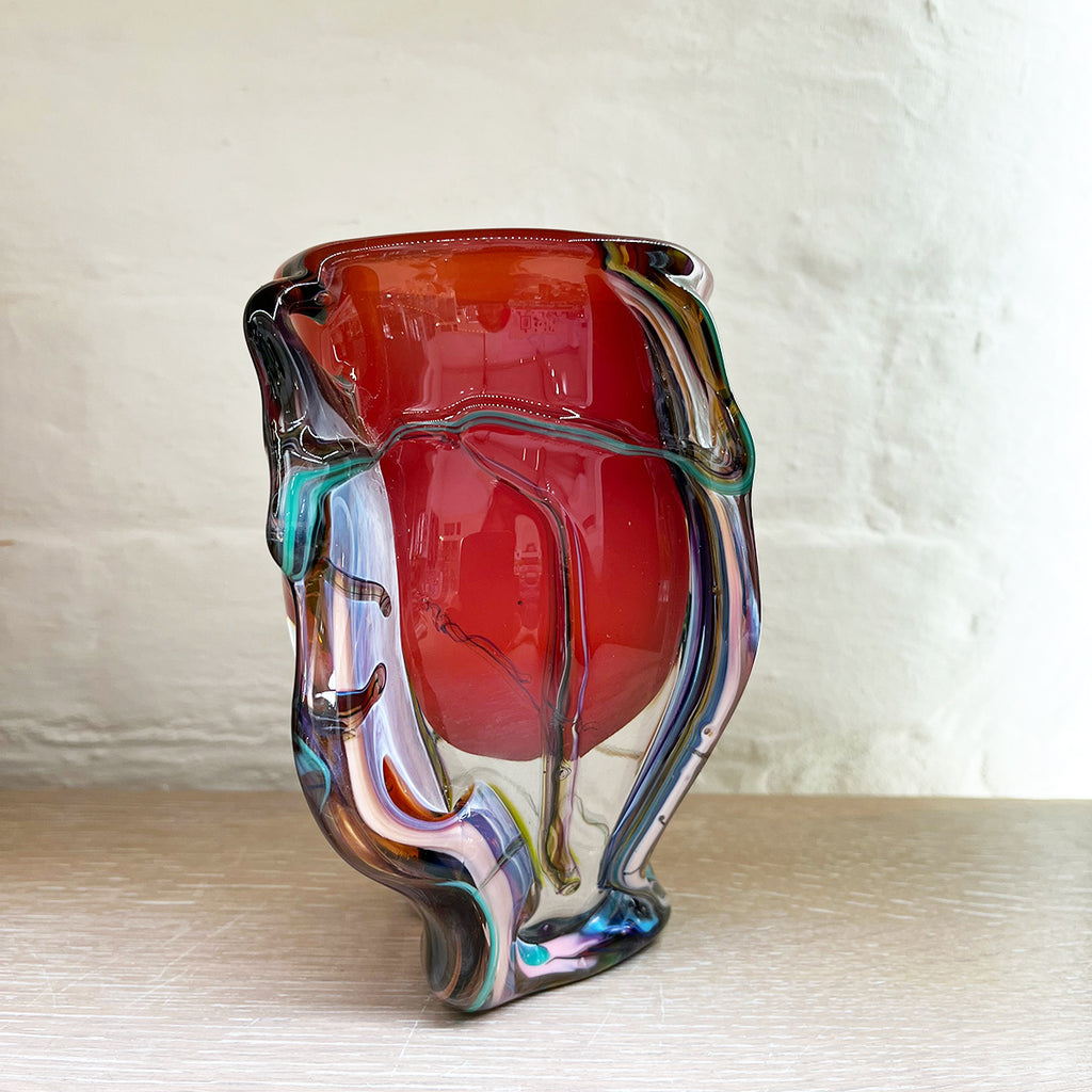 side view of stunning bowl by contemporary glass artist Will Shakspeare. The piece is inspired by trees and is predominantly red in colour with 'roots' in blues and a kaleidoscope of colours.