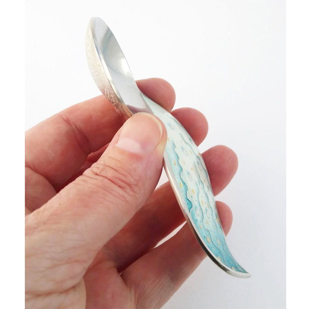 'Fizz' Spoon being held - this beautiful piece is formed by hand with hammers, and the enamel area on the handle is then hand engraved. Following from this the piece is enamelled and cloisonné wires alongside painted enamel details complete the design. By contemporary Silversmith Ruth Ball