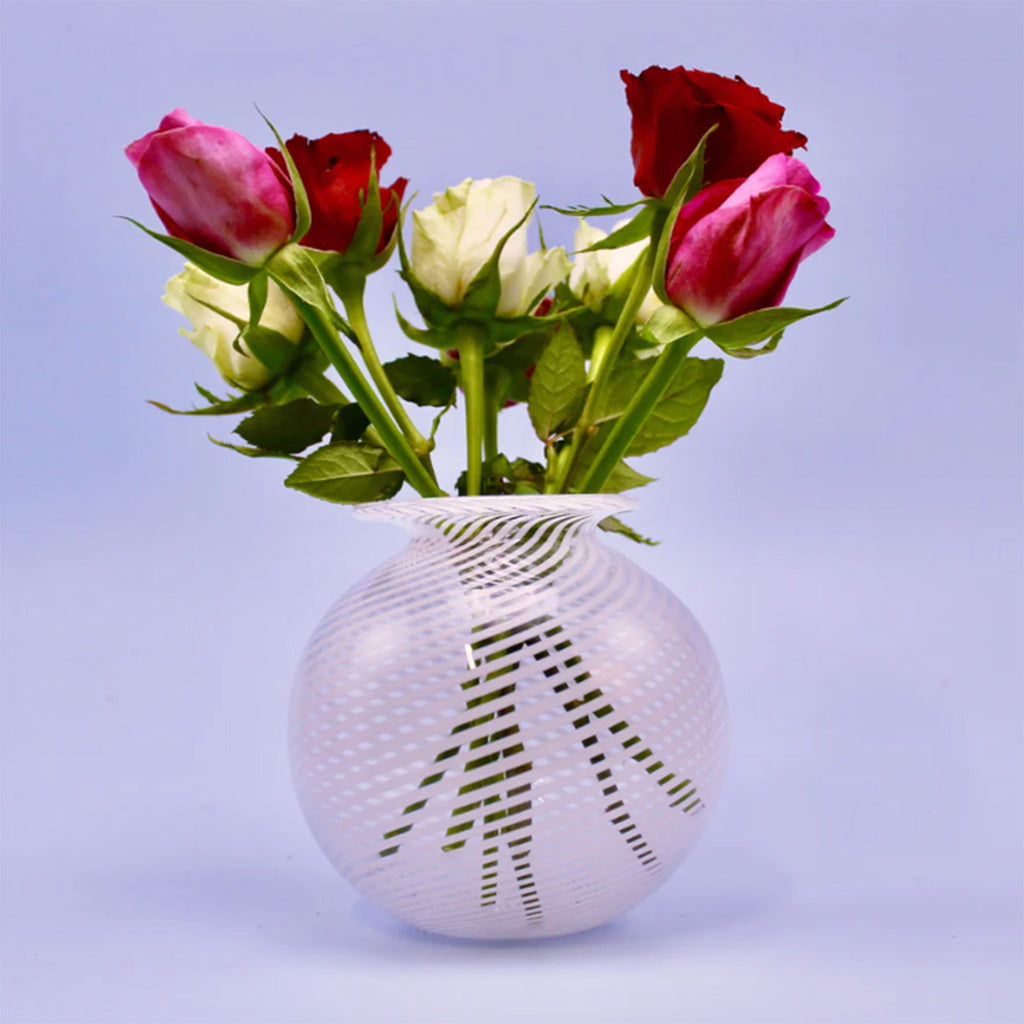 large round glass vase by Benefield Spencer Glass show with the distinctive filigrana style of blown glass with an alternating pattern of clear and white canes, holding a large bunch of roses