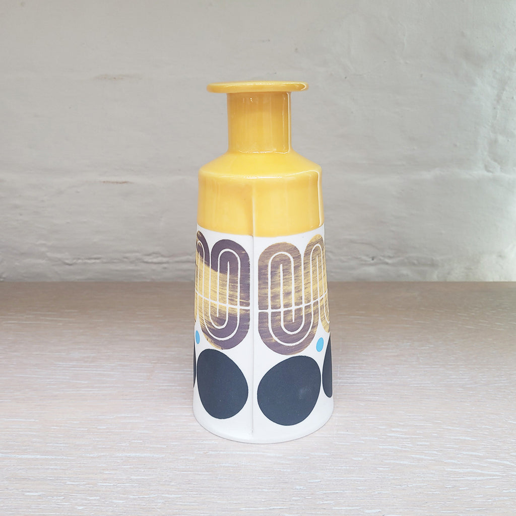 Slab-built porcelain ceramic bottle with predominently white background with black and purple pattern and a yellow top section. Back view
