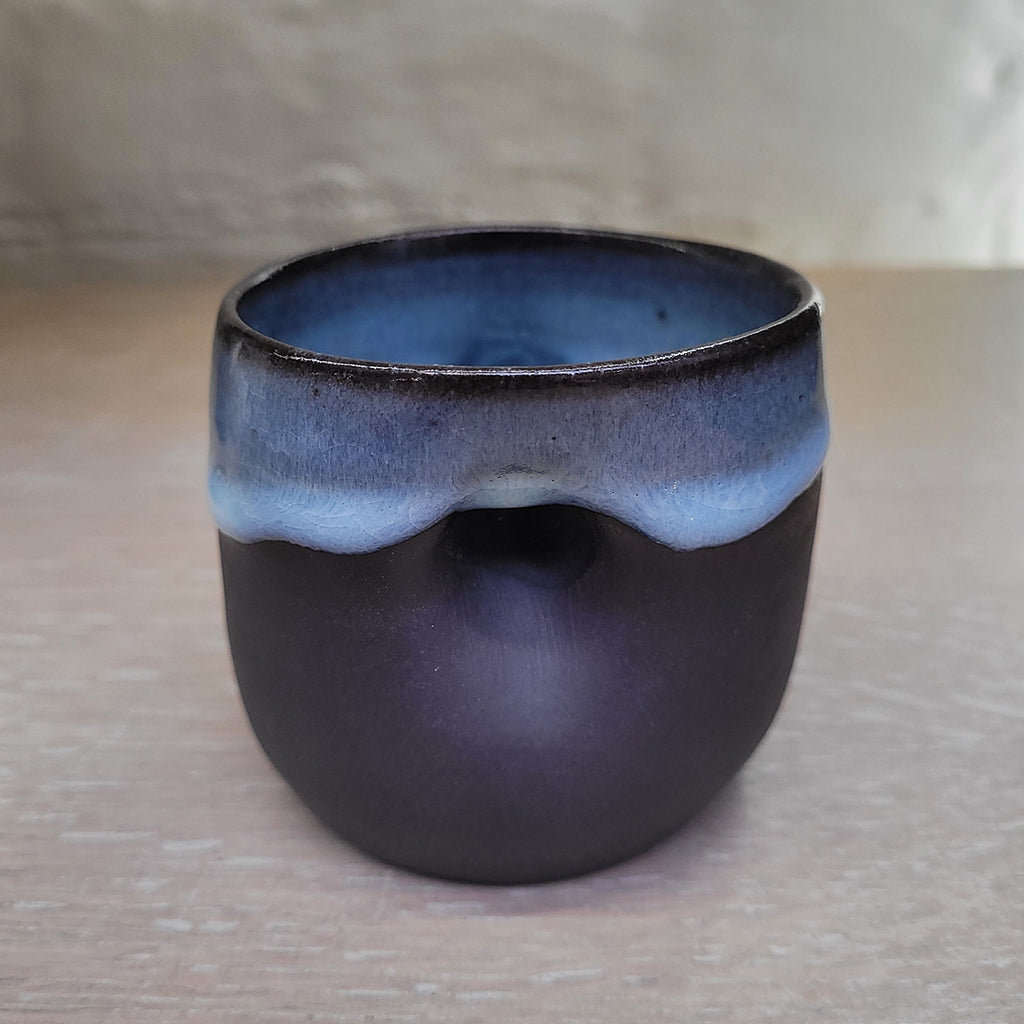 Rear view of black porcelain teacup with the Madonna's face in 3d relief featuring a blue glaze on the inside and dripping outside