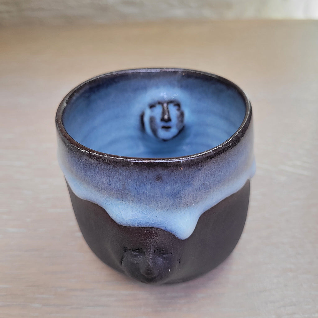 Black porcelain teacup with the Madonna's face in 3d relief on both the inside and outside.  There is a blue glazed internally and dripped around the outside