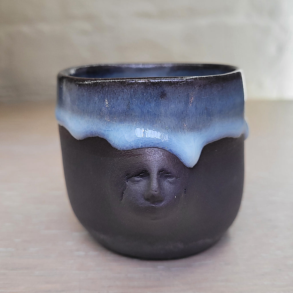 Black porcelain teacup with the Madonna's face in 3d relief pushed into the surface. Features a blue glaze inside and dripping on the external 