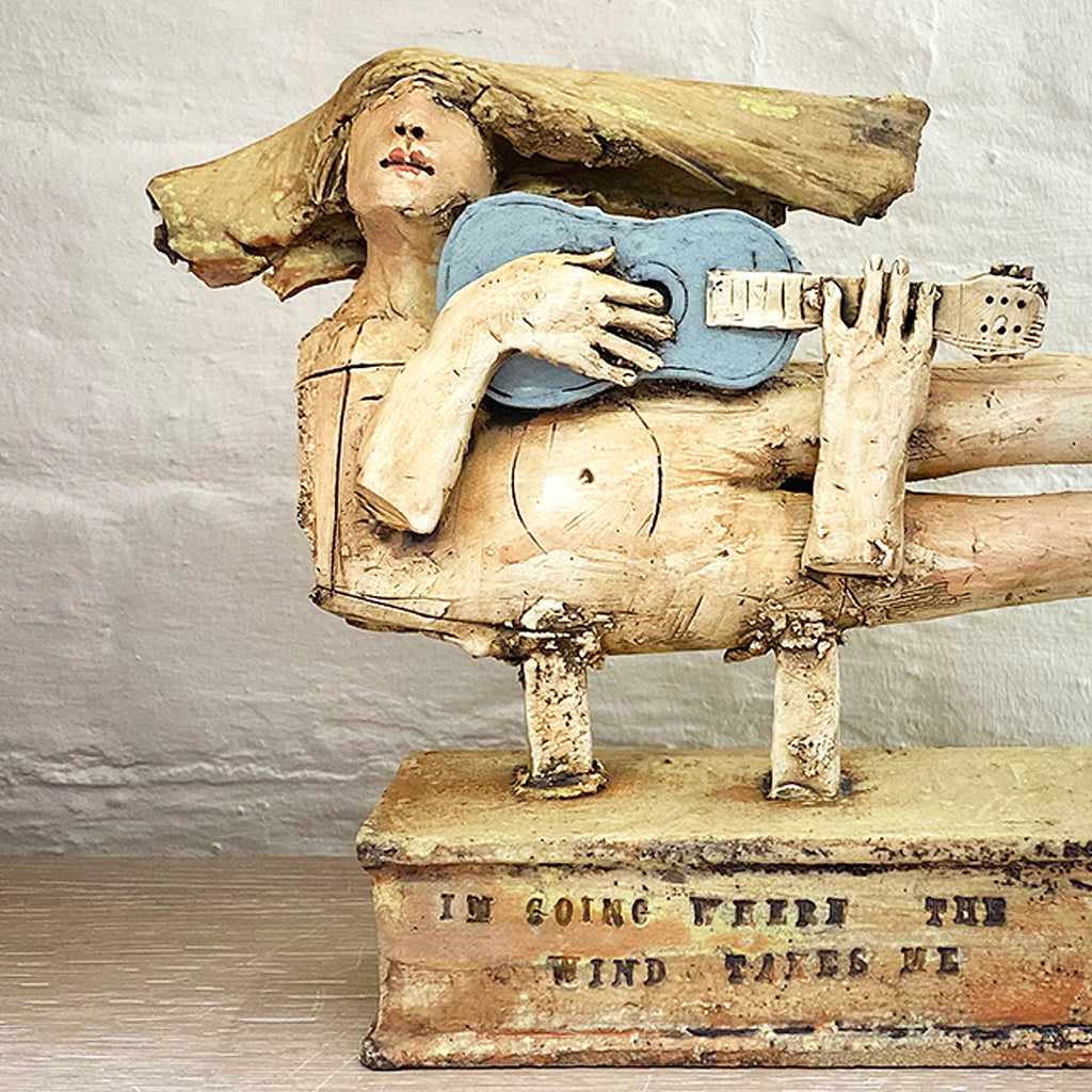 close up of sculpture of a flying figure playing a guitar inscribed with “I’m Going Where the Wind Takes Me” slab-built by contemporary ceramicist Christy Keeney