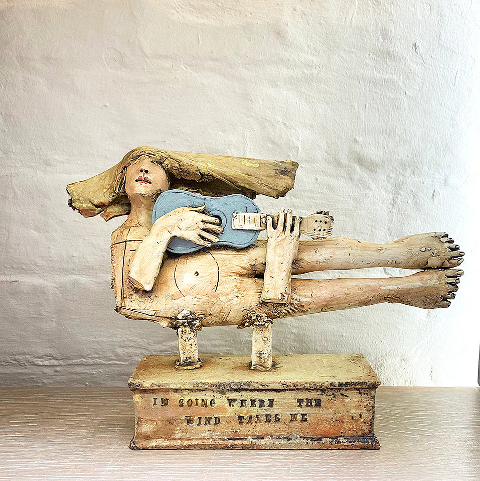 sculpture of a flying figure playing a guitar inscribed with “I’m Going Where the Wind Takes Me” slab-built by contemporary ceramicist Christy Keeney