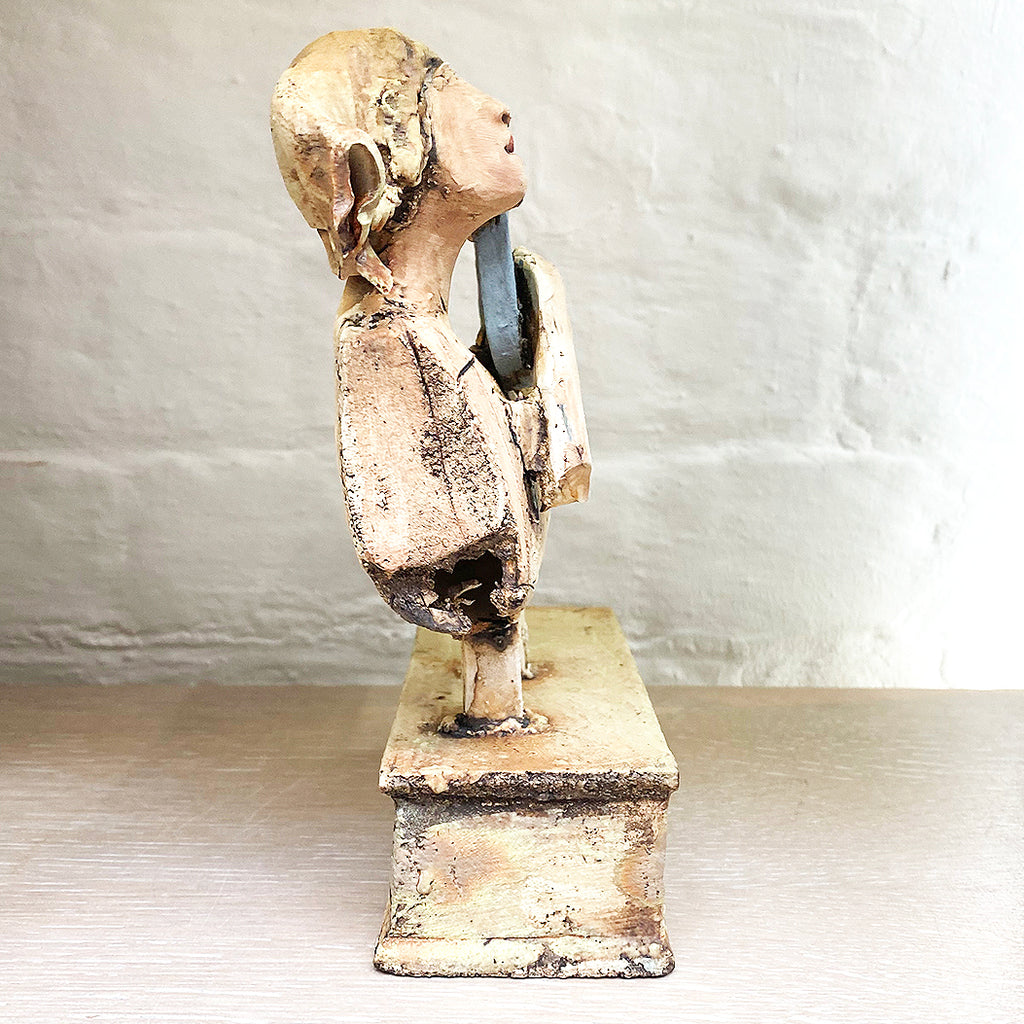 side view of sculpture of a flying figure playing a guitar inscribed with “I’m Going Where the Wind Takes Me” slab-built by contemporary ceramicist Christy Keeney