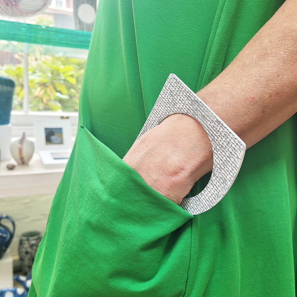 White and grey A-shaped bangle inspired by the Bauhaus design movement shown worn with a green dress. Made from linoleum and hand painted by Studio Ditto in Liverpool