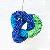 close up of one of pair of knotted paper earrings in tones of light blue, dark blue and green twisted throughout each other