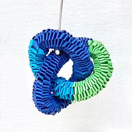 close up of one of pair of knotted paper earrings in tones of light blue, dark blue and green twisted throughout each other