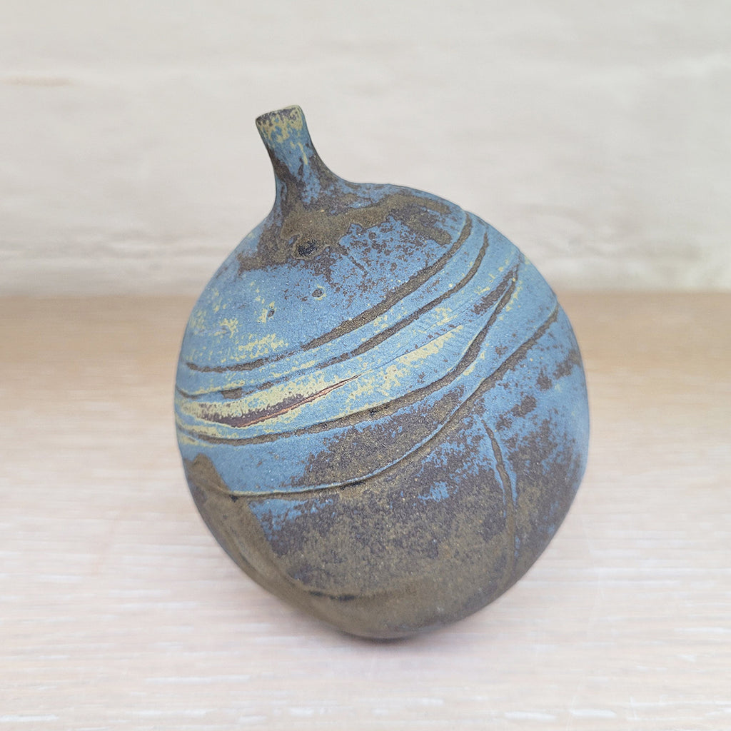 back view of a stunning piece of contemporary ceramic featuring texture, deep blues and ochres. Held inside this small stoneware bottle are porcelain seashells which give a gentle rattle when shaken
