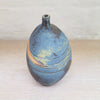 side view of a stunning piece of contemporary ceramic featuring texture, deep blues and ochres. Held inside this small stoneware bottle are porcelain seashells which give a gentle rattle when shaken
