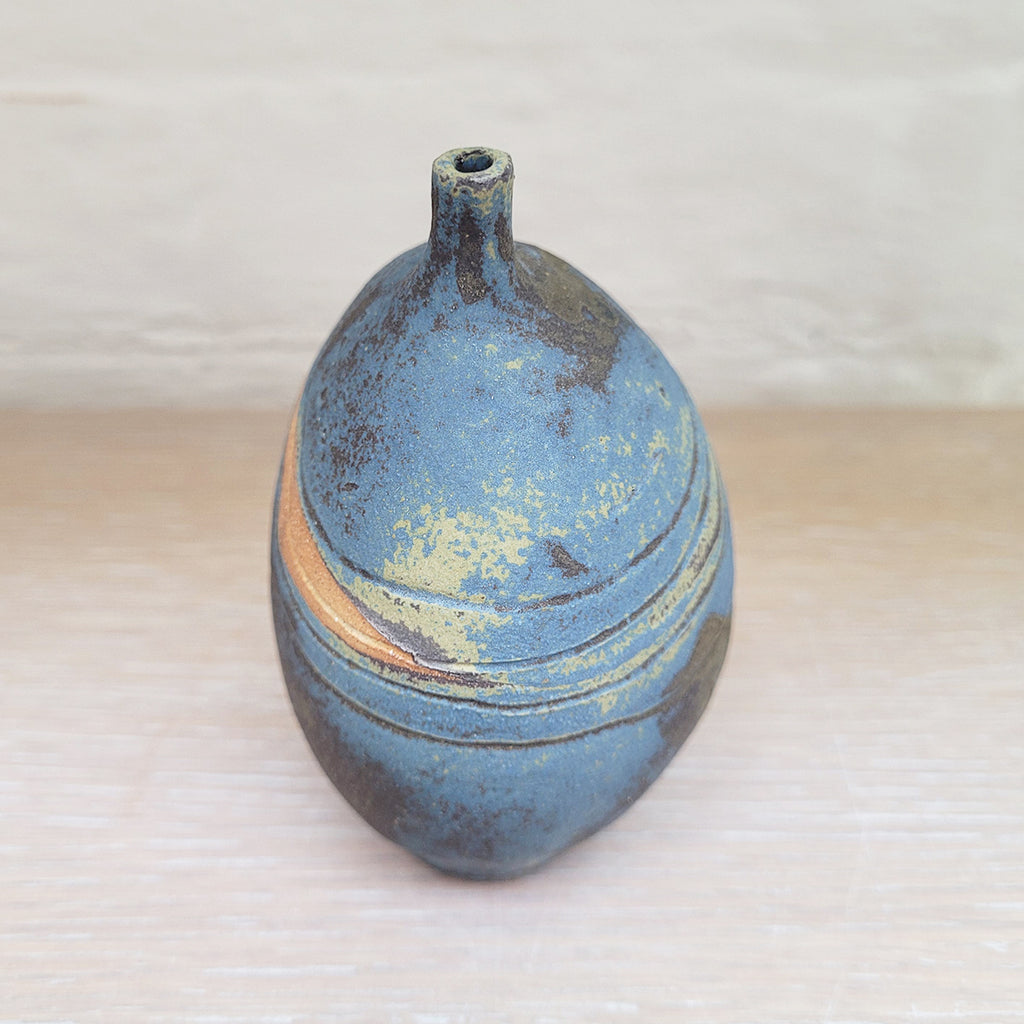 side view of a stunning piece of contemporary ceramic featuring texture, deep blues and ochres. Held inside this small stoneware bottle are porcelain seashells which give a gentle rattle when shaken