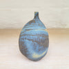 right side view of a stunning piece of contemporary ceramic featuring texture, deep blues and ochres. Held inside this small stoneware bottle are porcelain seashells which give a gentle rattle when shaken