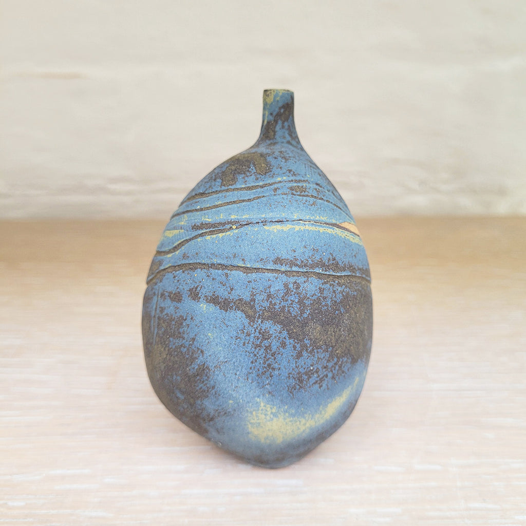 right side view of a stunning piece of contemporary ceramic featuring texture, deep blues and ochres. Held inside this small stoneware bottle are porcelain seashells which give a gentle rattle when shaken