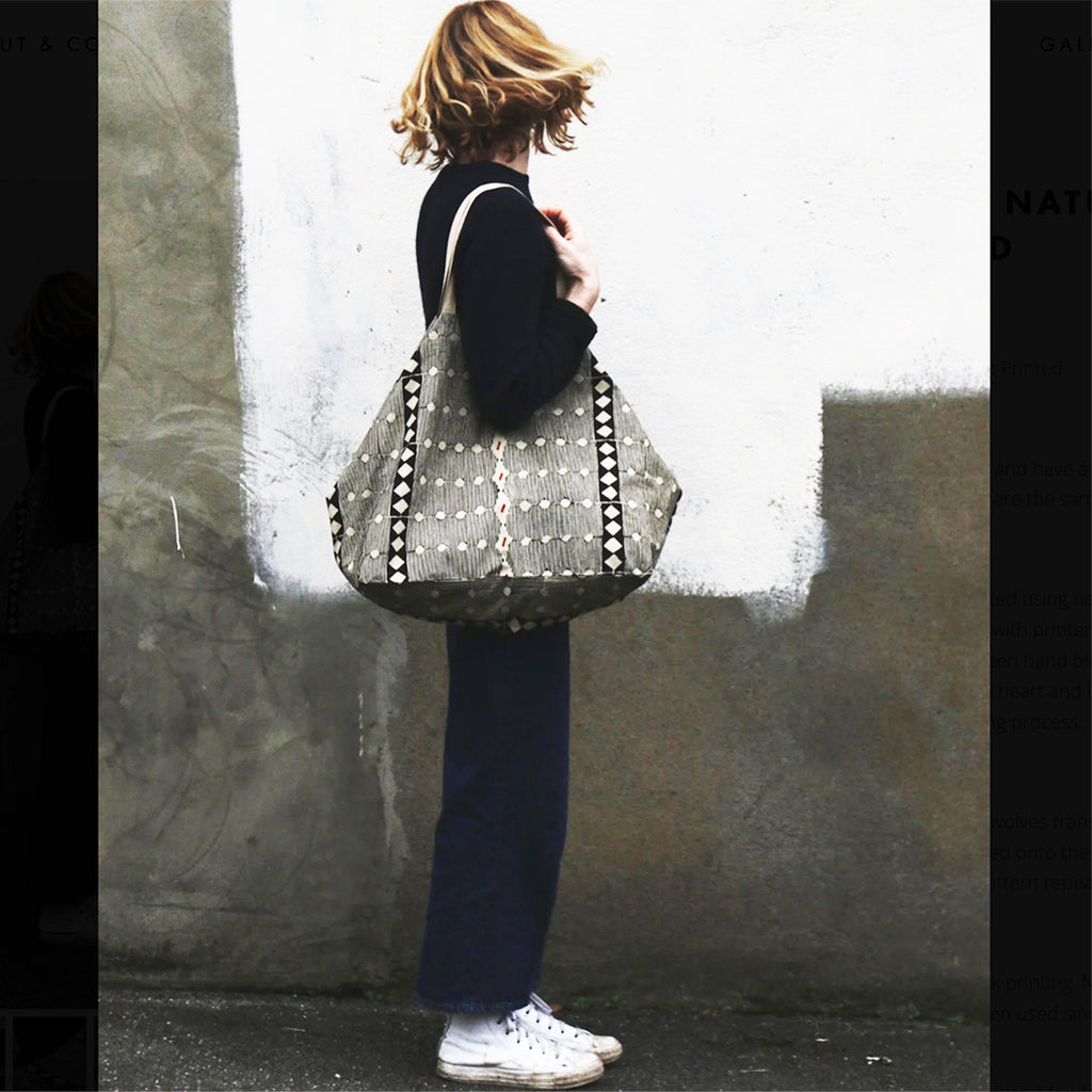 Person holding a Naturally dyed & Hand Block Printed Bag by Louisa Loakes against a textured wall.