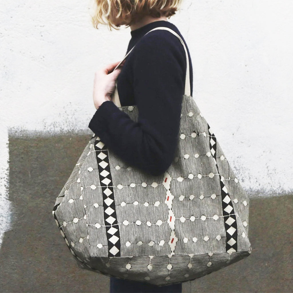 Close up of Person holding a Naturally dyed & Hand Block Printed Bag by Louisa Loakes against a textured wall.