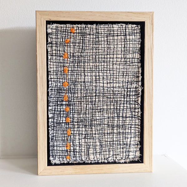 Framed textile art featuring a bold design comprised of orange dots in a stitched grid by Irish textile artist Patricia Kelly