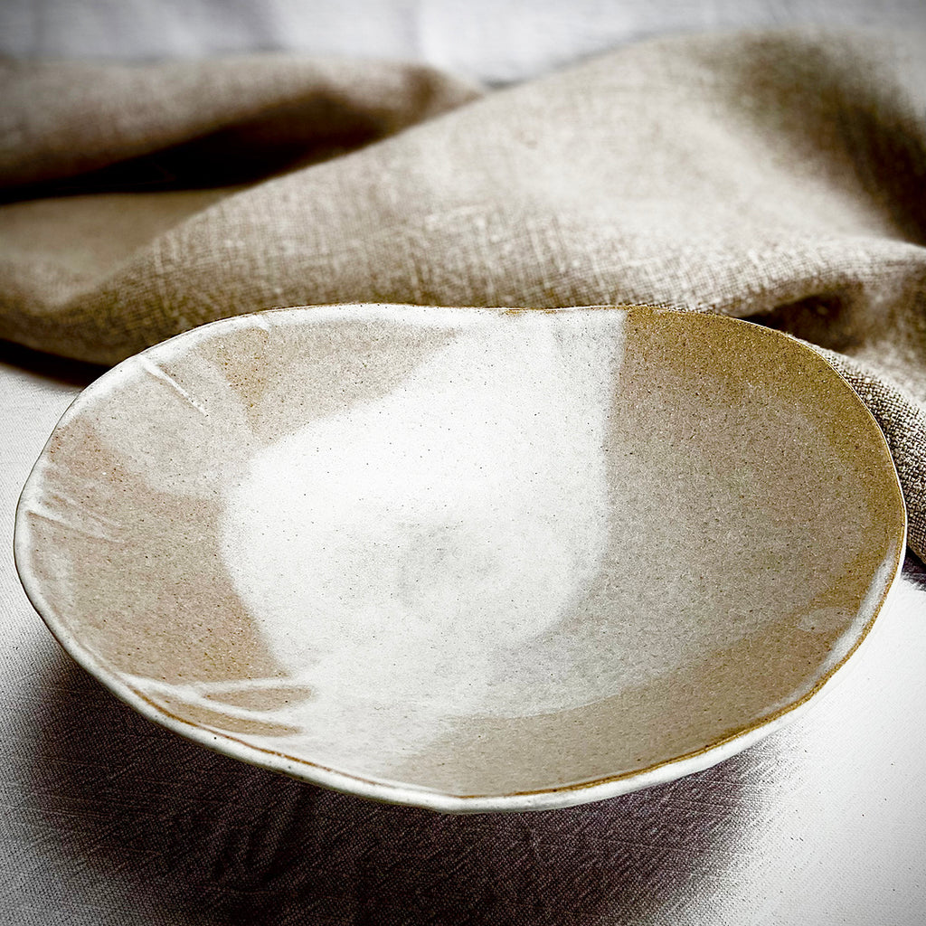 side top view of raised organic-shaped dish in a buff stoneware clay, simply finished with a loosely applied off-white matte glaze by contemporary ceramicist Sarah Bartlem