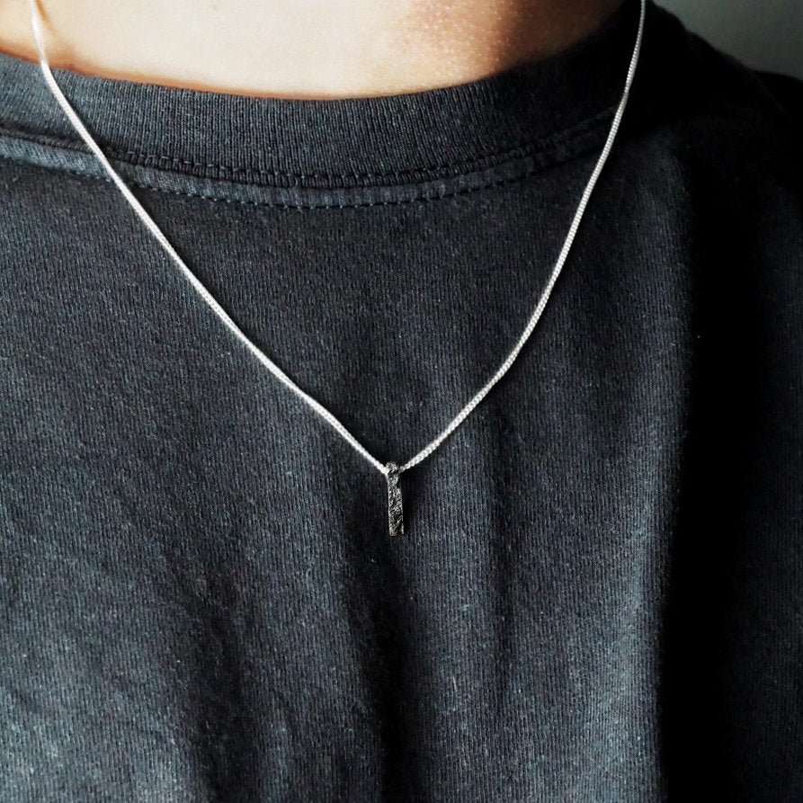 Person in black t-shirt wearing Ripples Pendant by Sam Holmes crafted from oxidised sterling silver with delicate undulations and surface textures