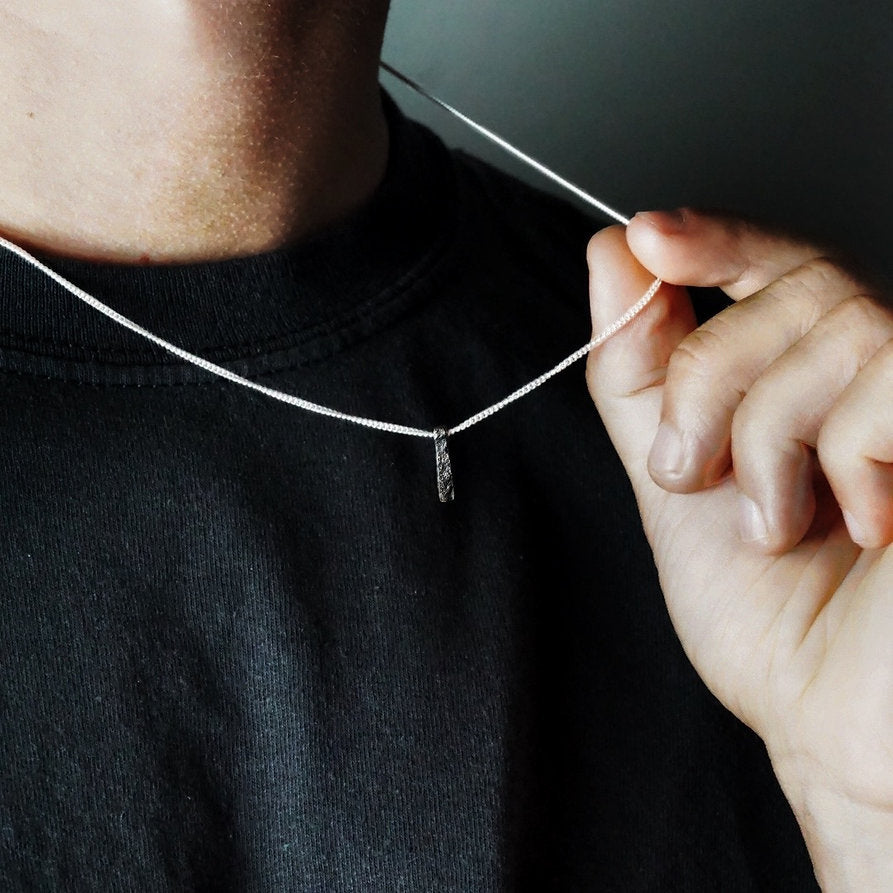 Person wearing and holding Ripples Pendant by Sam Holmes crafted from oxidised sterling silver with delicate undulations and surface textures