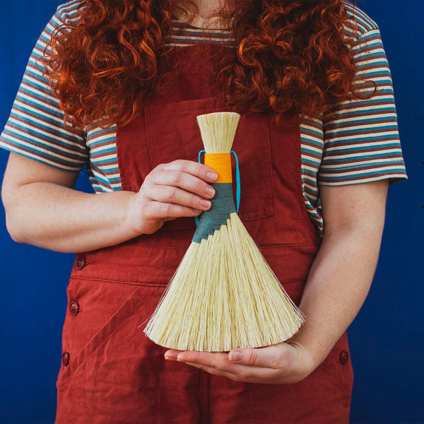 Person holding a Tampico brush in a striking Teal and gold - perfect for work surfaces in the home, workshop or garden. This brush is ideal for dusting or sweeping crumbs on kitchen tables and counters, among other uses. 