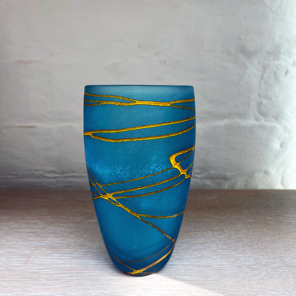 A medium small cone vase from contemporary glass worker Will Shakspeare's 'Random Trails' range, inspired by walking in the Elan Valley in Wales.  This vase is predominently aqua blue with threads of gold colour