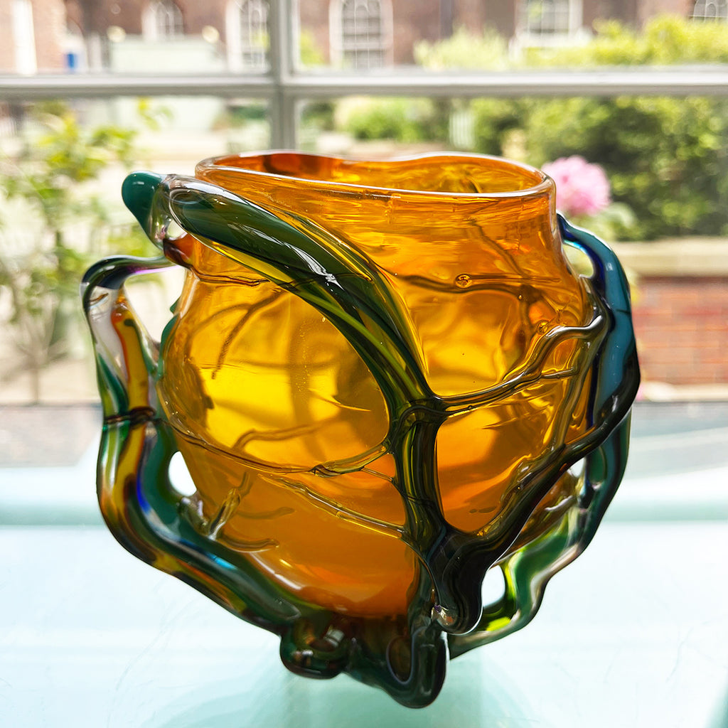 'roots' orange bowl by contemporary glass artist Will Shakspeare. The piece is inspired by trees and is predominantly orange in colour with green 'roots'. one of the country's most collected contemporary makers.  Shown in the Bluecoat Display Centre, contemporary craft gift shop