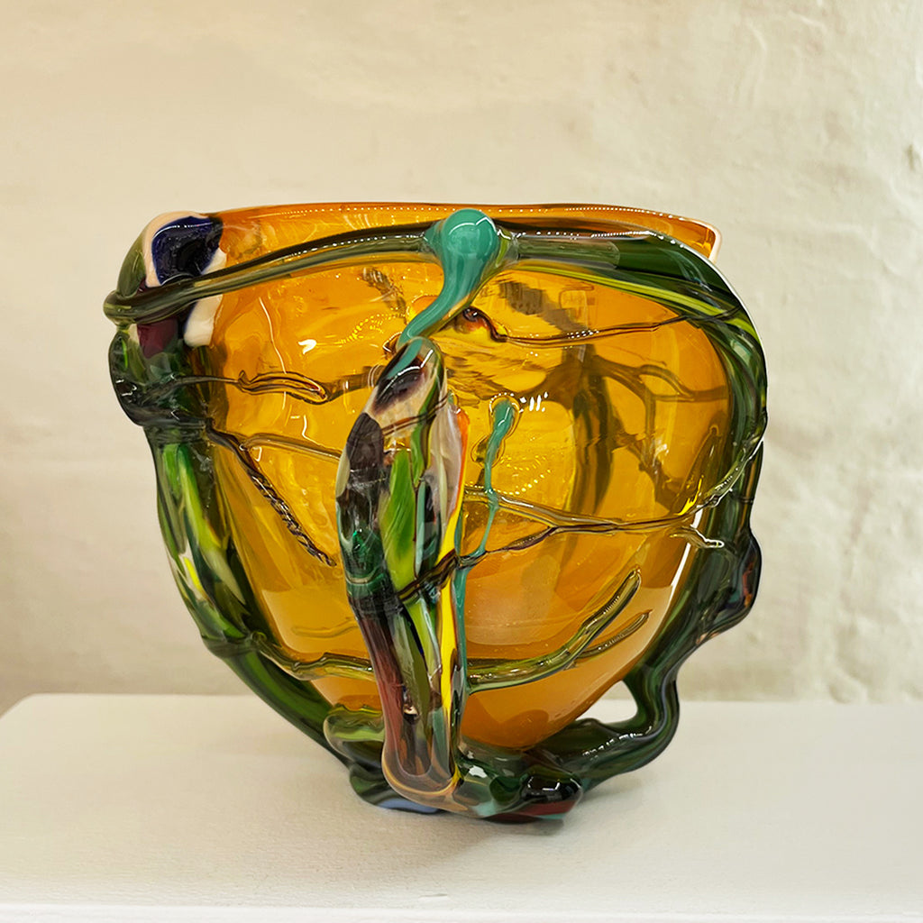 A small bowl by contemporary glass artist Will Shakspeare. The piece is inspired by trees and is predominantly orange in colour with green 'roots'. one of the country's most collected contemporary makers.