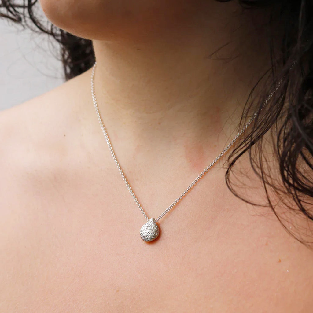 Model wearing Silver pebble pendant with an organic finish and hand-etched words in gold by contemporary jeweller Diana Porter