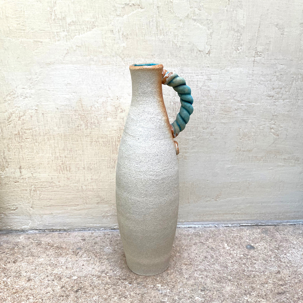 back view of slim stoneware bottle vase with a blue twisted handle. The base of the twisted handle is adorned with John Kershaw’s signature stamp