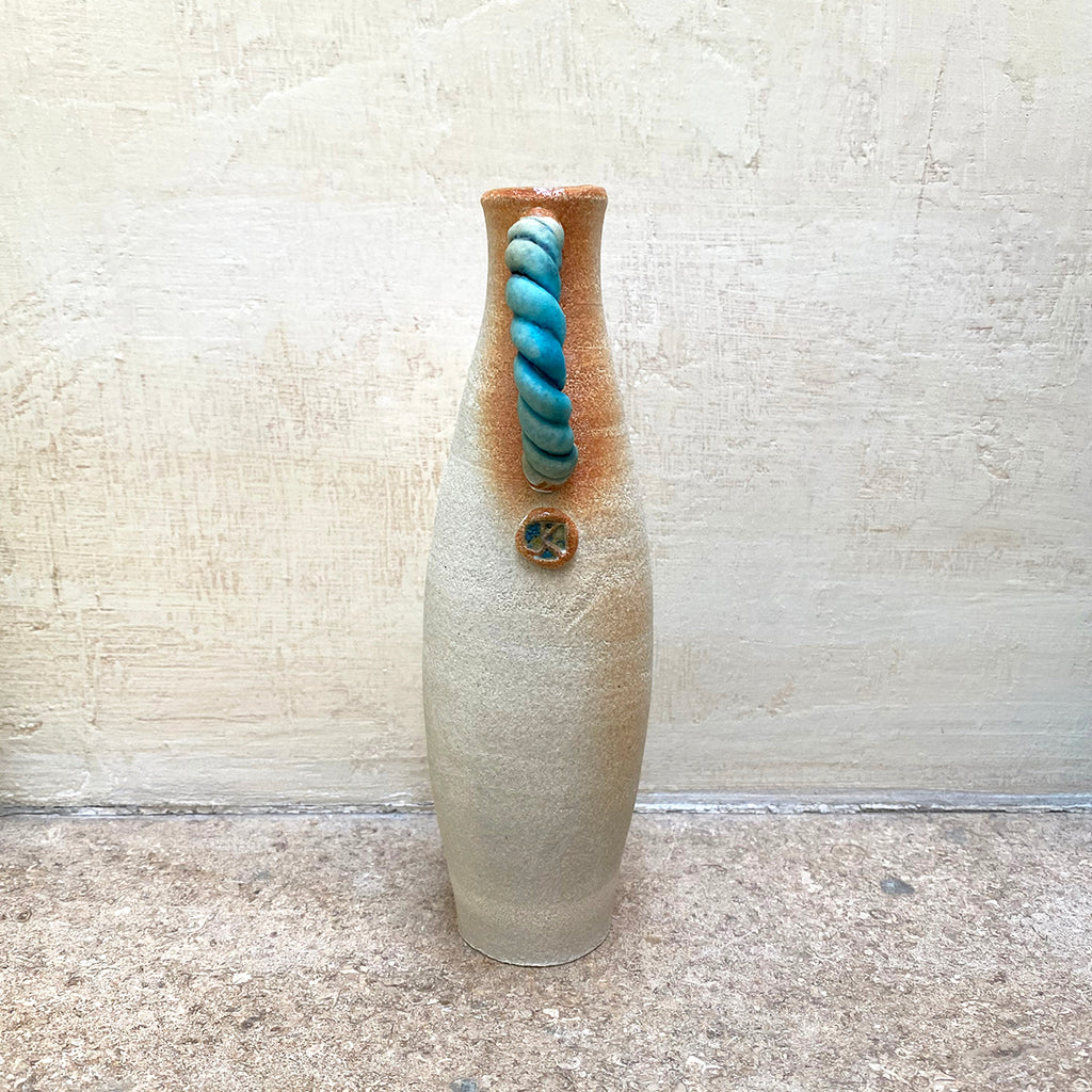 side view of slim stoneware bottle vase with a blue twisted handle. The base of the twisted handle is adorned with John Kershaw’s signature stamp