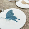 Teal Butterfly Wall Plaque by Tiffany Scull with a gold butterfly wall plaque in the distance