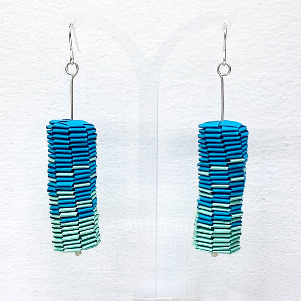 A pair of paper drop earrings are a vibrant aqua and teal gradient by Rike Lenzing