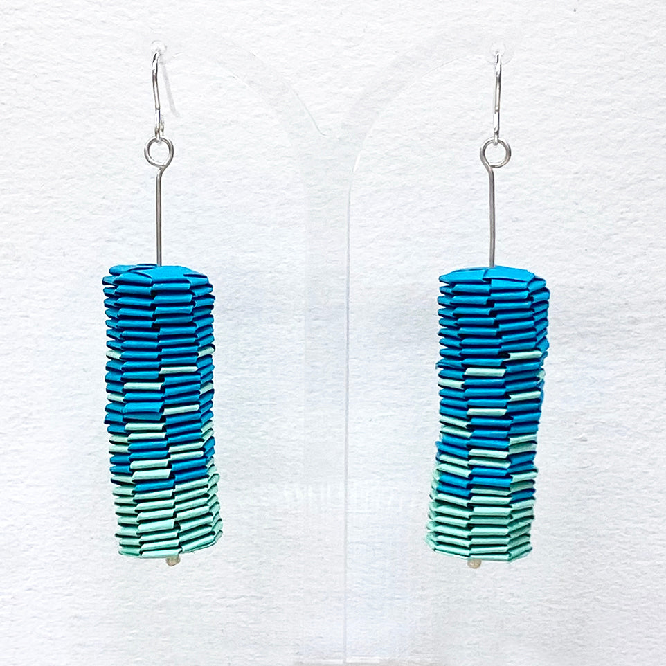 A pair of paper drop earrings are a vibrant aqua and teal gradient by Rike Lenzing