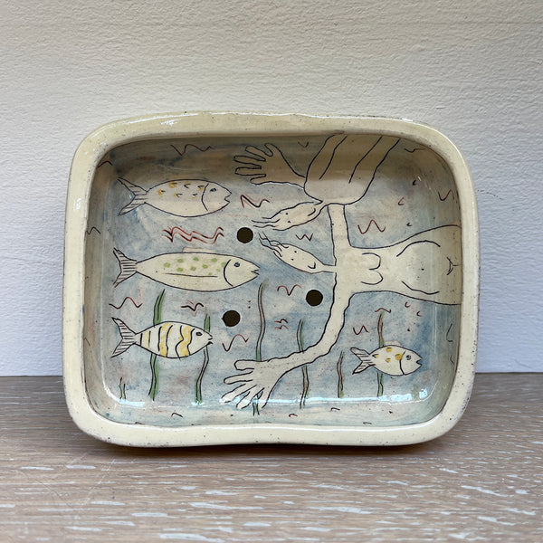 Blue soap dish, decorated with figurative illustrations using coloured slips, brushwork, stencils and sgraffito on red earthenware. Contemporary Ceramicist Vivienne Ross's unique illustrations contain an element of humour. This dish features 2 figures in a sea of fish and plants