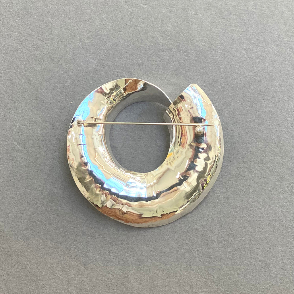 Back of a Beautiful Sterling Silver Swirled Round Brooch by irish Silversmith Kevin O’Dwyer on a grey background
