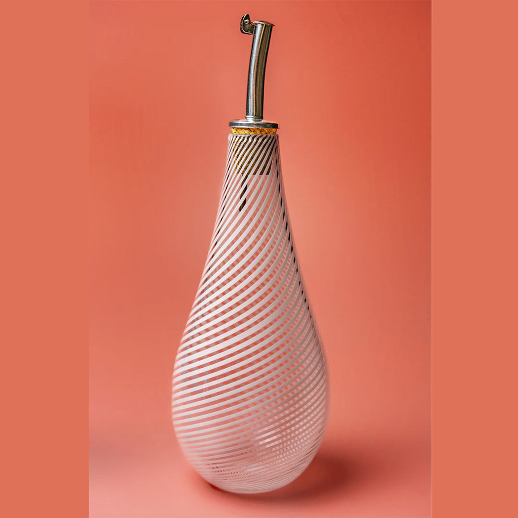 A detail shot of a small glass bottle for drizzling olive oil, fitted with a cork pouring spout and embodying the Benefield Spencer signature white filigrana cane pattern. 