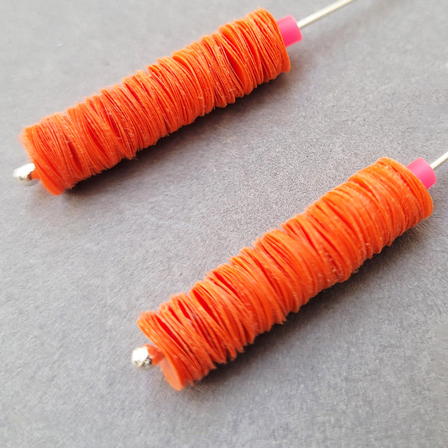 Detail of orange drop earrings made from recycled polythene bags with silver earring posts by contemporary jewellery designer Rachel Darbourne
