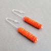 Side view of orange drop earrings made from recycled polythene bags with silver earring posts by contemporary jewellery designer Rachel Darbourne